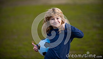 Boy child playing football on football field. Kid playing soccer show thumbs up success sign. Boy holding soccer ball Stock Photo
