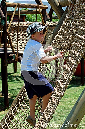 Boy climbing a rope ladder in playground Stock Photo