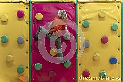 Boy climbs soft climbing wall. Child has fun in the childrens playroom. Soft room for games Stock Photo