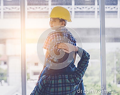 Boy in construction helmet sitting on father neck looking back with sunlight for father and son builder future concept Stock Photo