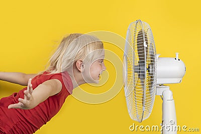 Boy cools off with ventilator. Portrait on yellow background. Summer heat Stock Photo