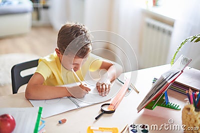 The boy does his homework at home. happy child at the table with school supplies concentrated writing in the retreat, doing Stock Photo