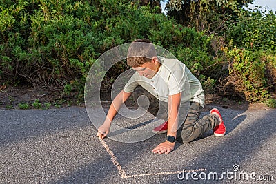 The boy draws on the pavement with colored chalk in the park. Drawing Stock Photo