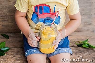 Boy drinking juicy smoothie from mango in glass mason jar with striped red straw on old wooden background. Healthy life concept, c