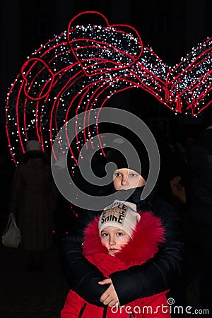 A boy embraces a girl against the background of the new year`s illumination of the arch of hearts Stock Photo