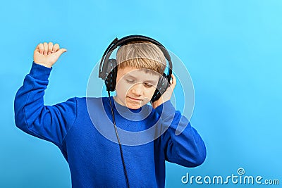 The boy enjoys listening to music through headphones and twitches while holding the headphones with one hand and waves around with Stock Photo