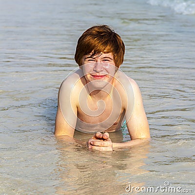 Boy enjoys lying in the spume of the tropical beach Stock Photo