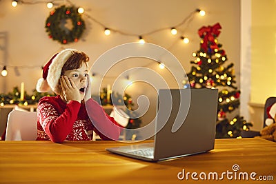 Boy in festive Santa costume feeling surprised during watching Christmas movie on laptop Stock Photo