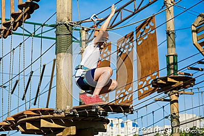 Boy in forest adventure park. Kid in orange helmet and white t shirt climbs on high rope trail. Climbing outdoor, amusement center Stock Photo