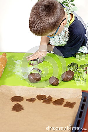 Boy forms and crushes the brown cake with his hand. Prepared cookies and a wooden rolling pin lie next to the counter. Stock Photo