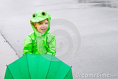 Boy In Frog Raincoat With a Green Umbrella Standing On a Street Stock Photo
