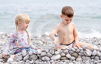 Boy and Girl Building Stone Wall on Rocky Beach Stock Photo