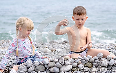 Boy and Girl Building Stone Wall on Rocky Beach Stock Photo