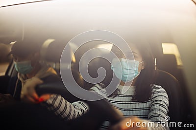 Boy and girl driving a car wearing sterile medical mask. Taxi driver with a passanger stuck in a traffic jam during coronavirus Stock Photo