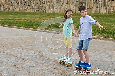 The boy and girl have joined hands and go on skateboards for a walk in the summer in the park Stock Photo