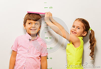 Boy and girl measure height by wall scale at home Stock Photo