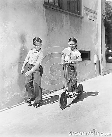 Boy and girl playing on a scooter and the other on roller blades Stock Photo