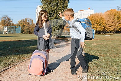 Boy and girl, primary school students with backpacks go to school. Sunny day background, road in the park Stock Photo