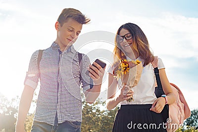 Boy and girl teenagers walking outdoor, couple smiling and talking. Sunny summer day, girl with bouquet of flowers Stock Photo