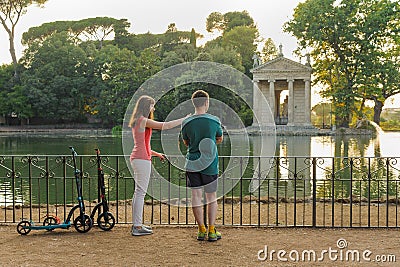 Boy and girl with their push scooters against the backdrop of the Tempio di Esculapio in the park Villa Borghese Stock Photo