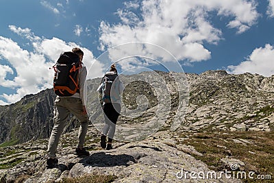 Young couple with big backpack walking to reach the top of the mountain during a sunny day Stock Photo