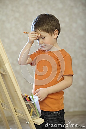 Boy With Hand On Forehead Standing In Front Of Easel Stock Photo