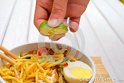 Boy hand squeezing lime on Malay Mee Rebus in the bowl with chopsticks on white table This dish is made of noodles ,vegetable,egg Stock Photo