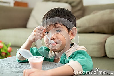 A boy happily uses a spoon to scoop up yogurt Stock Photo