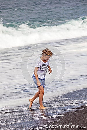 Boy has fun in the spume at the black beach Stock Photo
