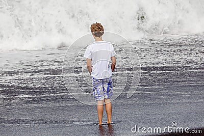 Boy has fun in the spume at the black volcanic beach Stock Photo