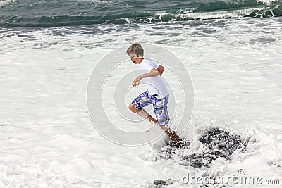 Boy has fun in the spume at the black volcanic beach Stock Photo