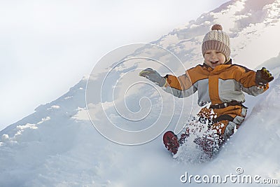 Boy in hat and orange jumpsuit slides off snow slide on back. Portrait. Close-up. Winter day Stock Photo
