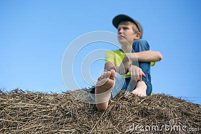 The boy on the haystack. Bare feet. Blue sky. Summer day Stock Photo