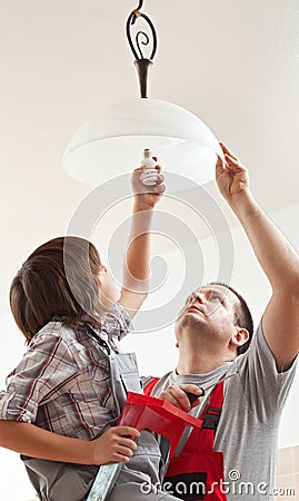 Boy helping father mounting a ceiling lamp - screwing in the lightbulb Stock Photo