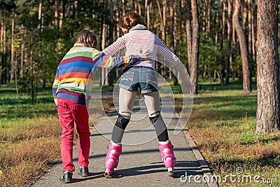 The boy helps the girl to roller-skate in the park. Brother supp Stock Photo