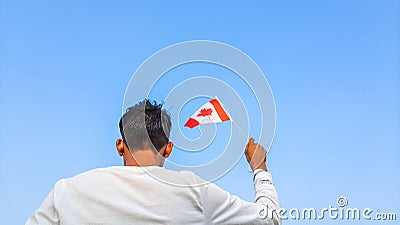 Boy holding Canada flag against clear blue sky. Man hand waving Canadian flag view from back, copy space Stock Photo