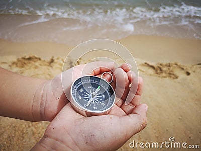 A boy holding a compass showing the direction point to north facing the ocean. Stock Photo