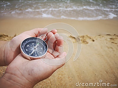 A boy holding a compass showing the direction point to north facing the ocean. Stock Photo
