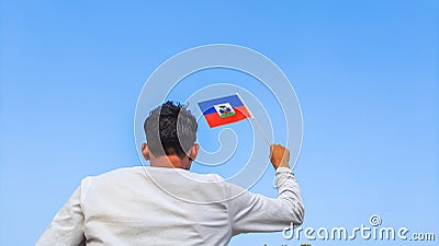 Boy holding Haiti flag against clear blue sky. Man hand waving Haitian flag view from back, copy space Stock Photo