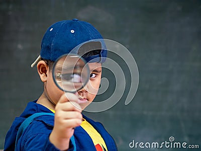 The boy holding the magnifying glass in front of blackboard. Back to School, Education Concept. Stock Photo