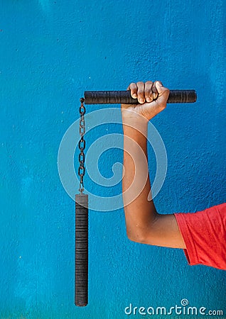 Boy holding Nunchaku on his hand on Blue background. Black nunchaku training for beginner. Hot Tactical Gear Martial Arts Stock Photo