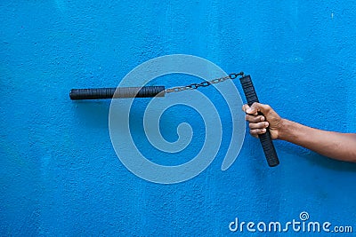 Boy holding Nunchaku on his hand isolated on Blue background. Black nunchaku training for beginner. Hot Tactical Gear Martial Arts Stock Photo