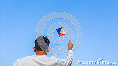 Boy holding Philippines flag against clear blue sky. Man hand waving Filipino flag view from back, copy space Stock Photo