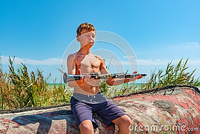 The boy holds a black clarinet in his hands, comprehending Zen sitting on an old wooden boat on the beach. Stock Photo