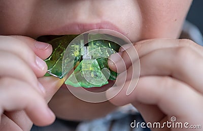 The boy inserts an orthodontic plate into his mouth to correct the malocclusion.green plastic orthodontic plate in the hands of a Stock Photo
