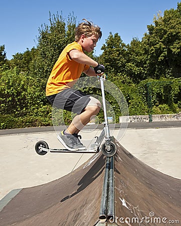 Boy is jumping with a scooter over a spine in the skate parc and Stock Photo