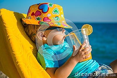 Boy kid in armchair with juice glass on beach Stock Photo