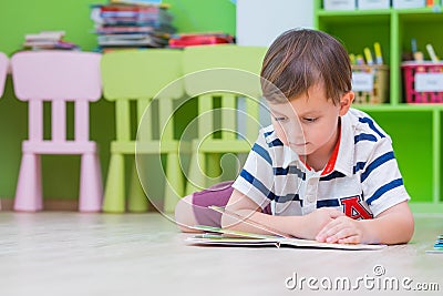 Boy kid lay down on floor and reading tale book in preschool li Stock Photo