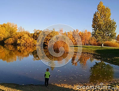 Boy by lake with fall colors in trees. Editorial Stock Photo