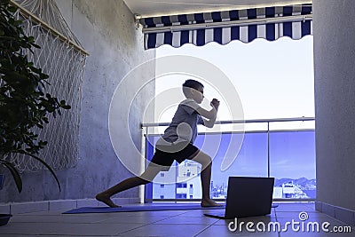 Boy with laptop computer doing sport exercises on balcony. Sport, healhty lifestyle, active leisure at home Stock Photo
